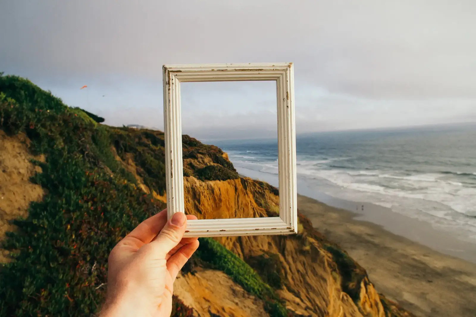 Eine Hand hält einen leeren Bilderrahmen vor die Küste und das Meer